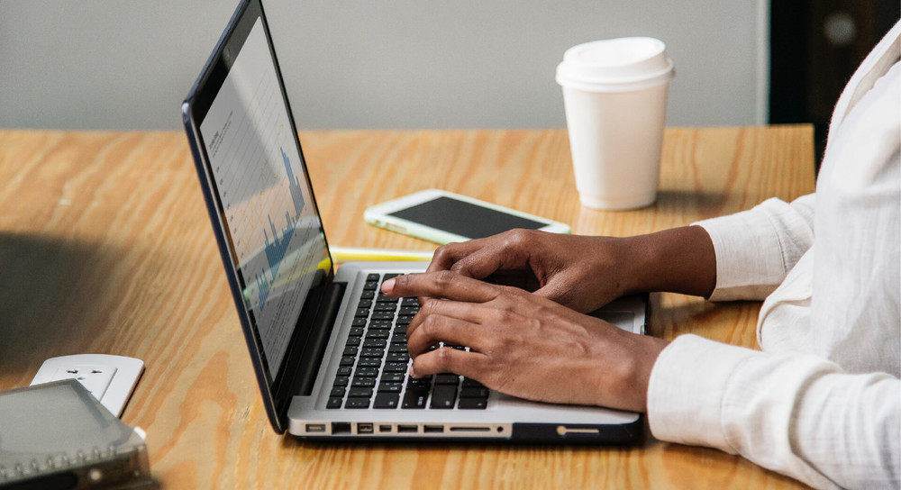Person typing on a laptop during work with an iphone and coffee
