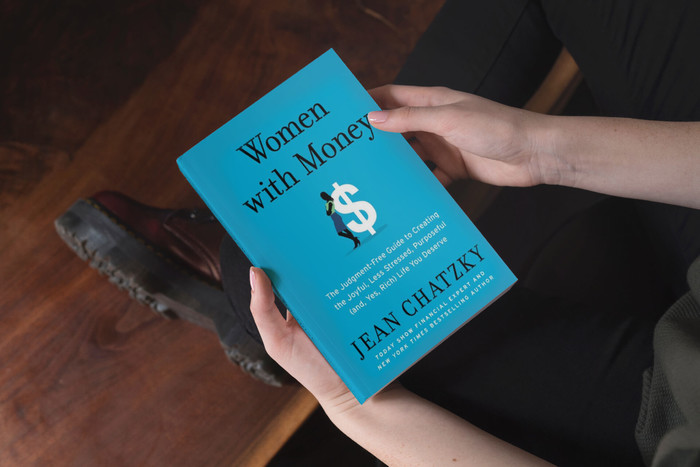 A person holding the book Women with Money in their arms while sitting