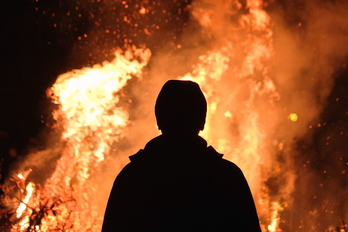 Silhouette man wearing a jacket and hat staring at a fire